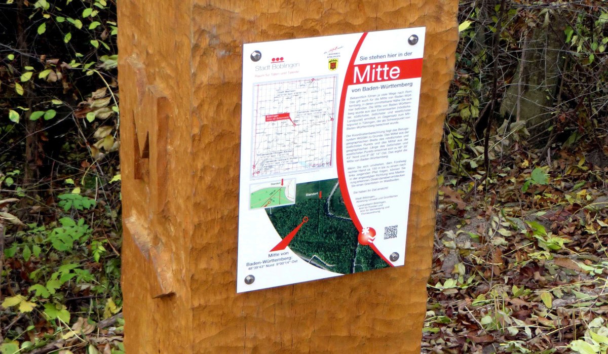 Ein hölzerner Wegweiser im Wald markiert die "Mitte von Baden-Württemberg". Ein Schild mit Karte und Text ist darauf befestigt., © Schwäbischer Albverein, Ortsgruppe Böblingen