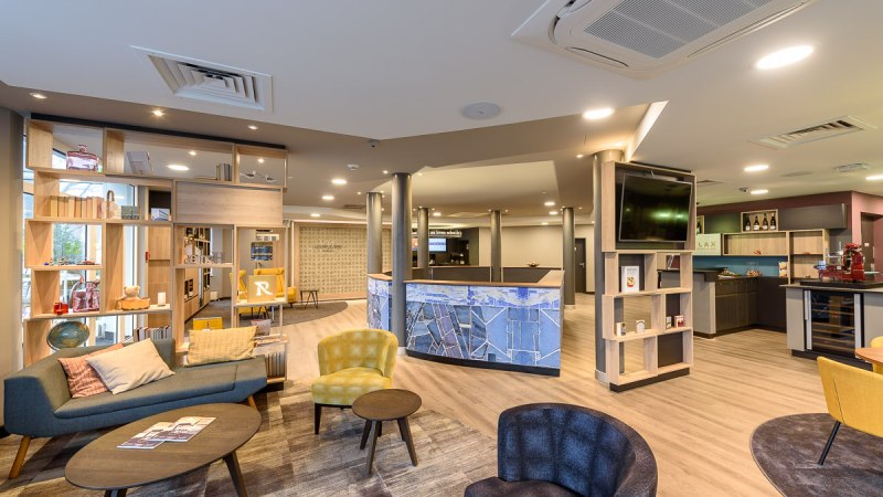 Moderne Hotellobby mit gem&uuml;tlichen Sitzgelegenheiten, Regalen und einer Rezeption. Helle Beleuchtung und stilvolle Einrichtung dominieren den Raum., &copy; TOMAS