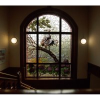 Ein kunstvolles Buntglasfenster mit Kranichen und Sonnenaufgang in einem historischen Treppenhaus, beleuchtet von zwei Wandlampen., &copy; Stadt G&ouml;ppingen