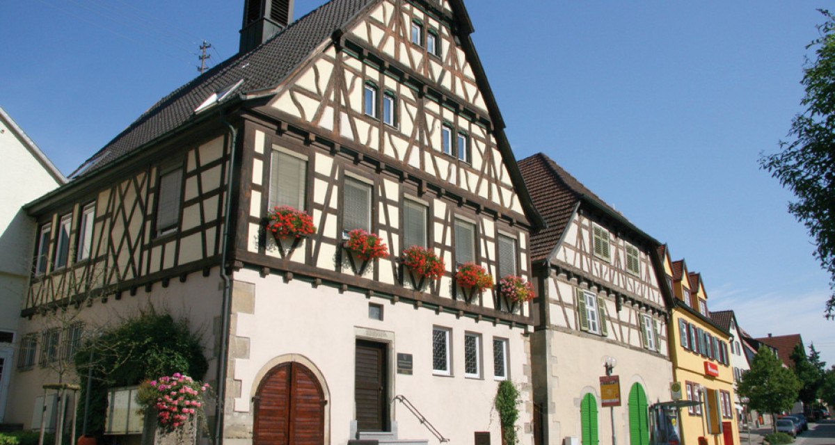 Fachwerk-Rathaus in Oberriexingen mit Blumen an den Fenstern, daneben weitere bunte Gebäude. Blauer Himmel im Hintergrund., © Land der 1000 Hügel - Kraichgau-Stromberg