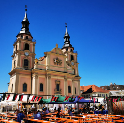 Ein belebter Marktplatz mit Festzelt und bunten Fahnen vor einer barocken Kirche unter klarem, blauem Himmel., &copy; Marktplatzfest Ludwigsburg GbR