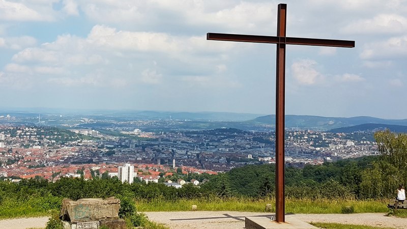 Blick vom Birkenkopf in Stuttgart mit einem großen Kreuz im Vordergrund und der Stadt im Hintergrund unter einem bewölkten Himmel., © Stuttgart-Marketing GmbH Blick vom Birkenkopf in Stuttgart mit einem großen Kreuz im Vordergrund und der Stadt im Hintergrund unter einem bewölkten Himmel., © Stuttgart-Marketing GmbH