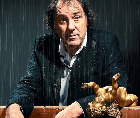 Ein Mann in einem nassen Anzug steht unter Regen, mit einem goldenen Engel auf einem Tisch vor ihm., © Veranstaltungsring Metzingen e.V. Ein Mann in einem nassen Anzug steht unter Regen, mit einem goldenen Engel auf einem Tisch vor ihm., © Veranstaltungsring Metzingen e.V.