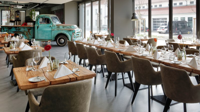 Ein modernes Restaurant mit Holztischen, eleganten Stühlen und einem alten blauen Truck als Dekoration. Große Fenster lassen viel Licht herein., © V8 Hotel, Frank Hoppe Ein modernes Restaurant mit Holztischen, eleganten Stühlen und einem alten blauen Truck als Dekoration. Große Fenster lassen viel Licht herein., © V8 Hotel, Frank Hoppe