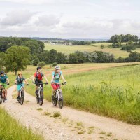 Vier Radfahrer fahren auf einem Feldweg durch eine grüne, hügelige Landschaft. Der Himmel ist bewölkt., © Schwäbische Alb Tourismusverband e.V.