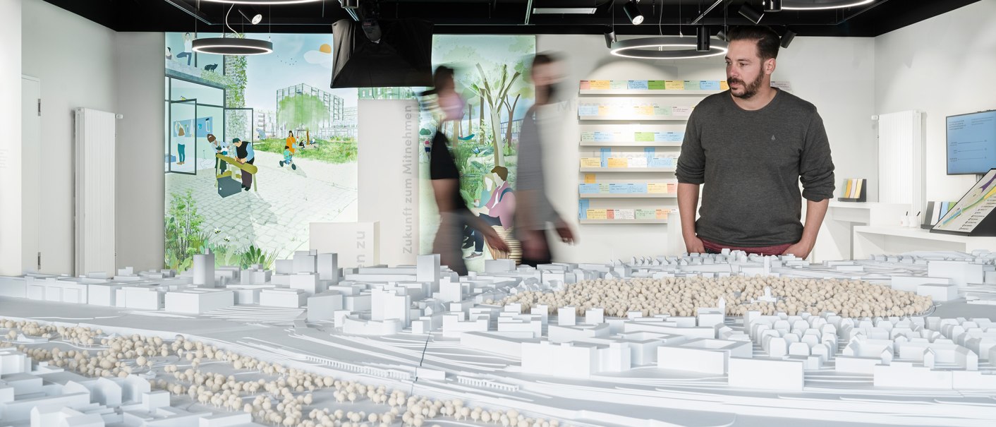 Ein Mann betrachtet ein Architekturmodell in einer Ausstellung. Im Hintergrund sind Illustrationen und Notizen an der Wand zu sehen., © Stadt Stuttgart / Dominique Brewing