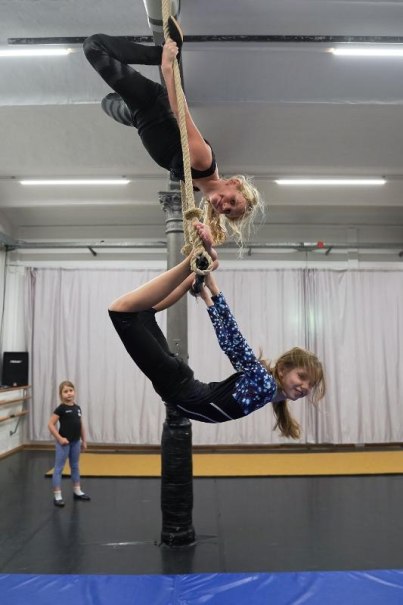Zwei Mädchen üben Luftakrobatik an einem Seil in einer Turnhalle, während ein weiteres Kind zuschaut., © Kunstschule Labyrinth Zwei Mädchen üben Luftakrobatik an einem Seil in einer Turnhalle, während ein weiteres Kind zuschaut., © Kunstschule Labyrinth