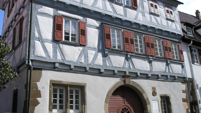 Ein traditionelles Fachwerkhaus mit roten Fensterl&auml;den und einem gro&szlig;en Holztor. Der Himmel ist blau mit einigen Wolken., &copy; Stadtmarketing Leonberg