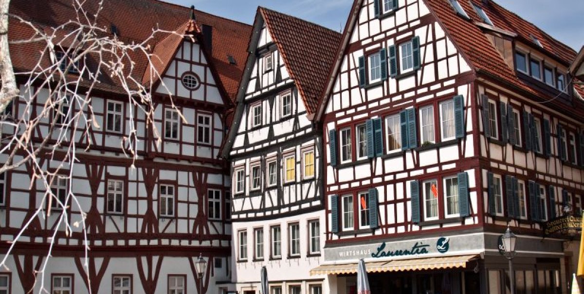 Fachwerkhäuser mit roten Dächern und blauen Fensterläden. Vor dem Wirtshaus Laurentia sitzen Menschen im Freien bei sonnigem Wetter. Fachwerkhäuser mit roten Dächern und blauen Fensterläden. Vor dem Wirtshaus Laurentia sitzen Menschen im Freien bei sonnigem Wetter.