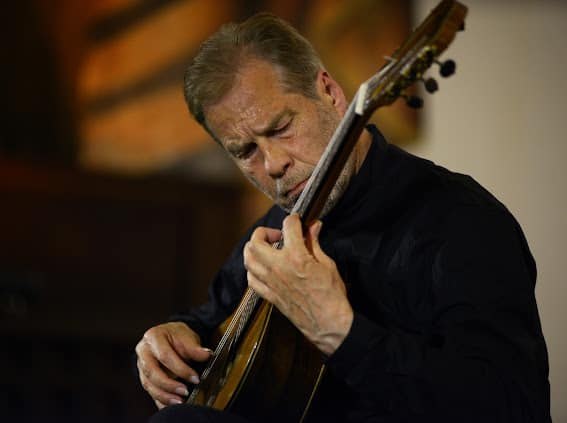 Ein Gitarrist spielt konzentriert auf einer Akustikgitarre während eines Konzerts. Der Hintergrund ist unscharf und warm beleuchtet. Ein Gitarrist spielt konzentriert auf einer Akustikgitarre während eines Konzerts. Der Hintergrund ist unscharf und warm beleuchtet.