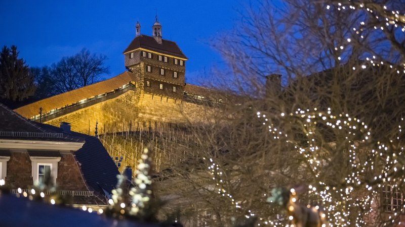 Die Esslinger Burg leuchtet in der Abenddämmerung, umgeben von Bäumen mit Lichterketten. Ein festlicher Anblick in der blauen Stunde., © Esslingen Markt und Event GmbH (EME)