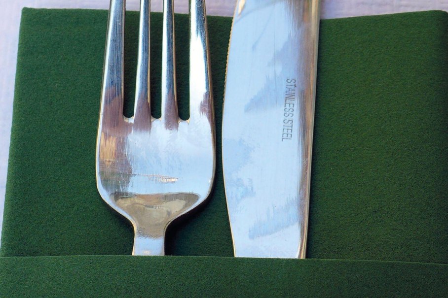 Eine Gabel und ein Messer aus Edelstahl liegen auf einer grünen Serviette. Das Messer ist mit 'STAINLESS STEEL' beschriftet., © Württembergische Landesbühne Esslingen Eine Gabel und ein Messer aus Edelstahl liegen auf einer grünen Serviette. Das Messer ist mit 'STAINLESS STEEL' beschriftet., © Württembergische Landesbühne Esslingen