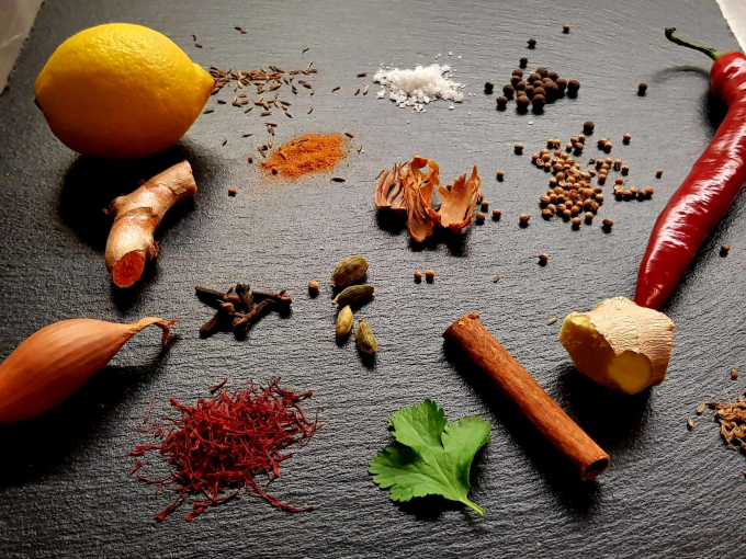 Zitrone, Ingwer, Chili, Schalotte, Zimtstange, Kardamom, Nelken, Safran, Petersilie und diverse Gewürze auf dunkler Oberfläche arrangiert., © Kultweine-Kochwelten-Kunstücke - Kochschule Sonja Lenz