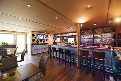 Moderne Bar mit langer Theke, Barhockern und Schallplatten-Dekor. Gemütliche Sitzbereiche und ein Fernseher an der Wand., © Bar Freddchen Moderne Bar mit langer Theke, Barhockern und Schallplatten-Dekor. Gemütliche Sitzbereiche und ein Fernseher an der Wand., © Bar Freddchen