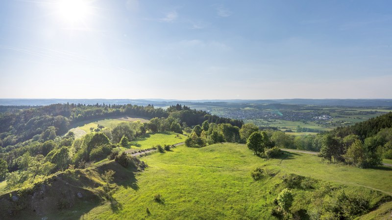 Weite Landschaft mit gr&uuml;nen H&uuml;geln und W&auml;ldern unter klarem Himmel, im Hintergrund eine Stadt. Die Sonne scheint hell., &copy; Stuttgart-Marketing GmbH, Martina Denker