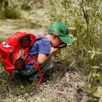 Ein Kind mit rotem Rucksack und gr&uuml;ner Kappe erkundet mit einer Lupe die Pflanzenwelt auf einer Wiese., &copy; Stadt N&uuml;rtingen