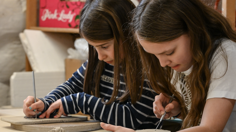 Zwei Mädchen konzentrieren sich auf das Formen von Ton in einem Workshop. Sie arbeiten mit Werkzeugen an Tonplatten., © Kunstschule Labyrinth Zwei Mädchen konzentrieren sich auf das Formen von Ton in einem Workshop. Sie arbeiten mit Werkzeugen an Tonplatten., © Kunstschule Labyrinth