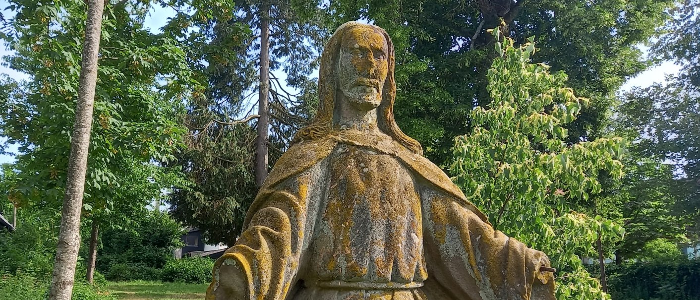 verwitterte Jesusfigur aus Stein, umgeben von Büschen und Bäumen., © Petra Natzkowski verwitterte Jesusfigur aus Stein, umgeben von Büschen und Bäumen., © Petra Natzkowski