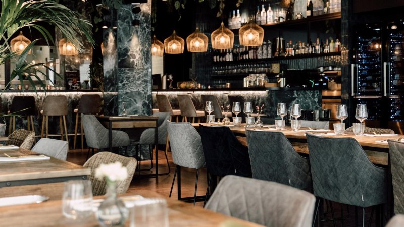 Elegantes Restaurant mit modernen Möbeln, gedeckten Tischen und stilvoller Bar im Hintergrund. Dezente Beleuchtung und Pflanzen sorgen für eine gemütliche Atmosphäre., © Malo Stuttgart - Lea Prestle