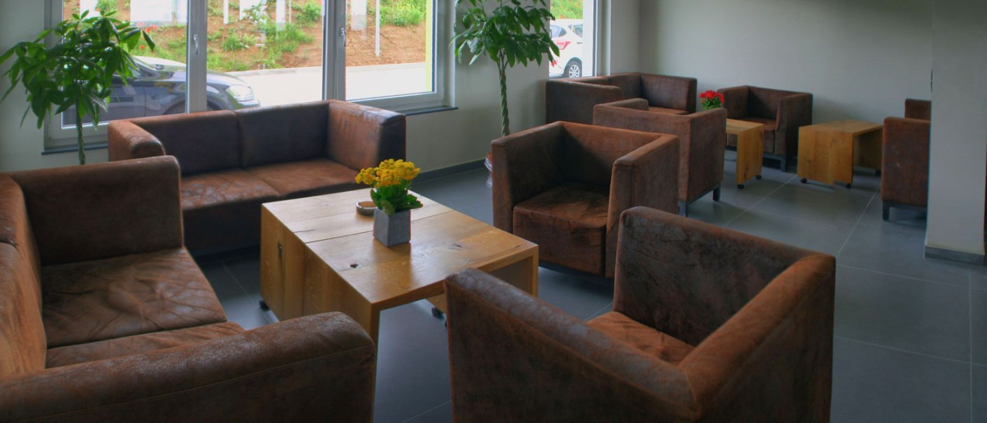 Gemütliche Raucherlounge mit braunen Ledersesseln, Holztischen und Pflanzen. Große Fenster lassen viel Licht herein., © TOMAS