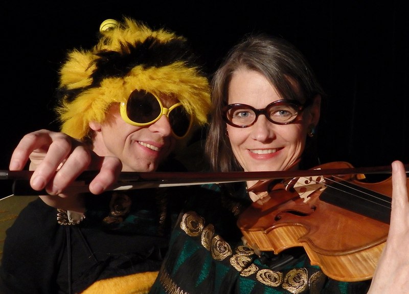 Zwei Personen posieren fröhlich; eine trägt eine gelbe Perücke und Sonnenbrille, die andere hält eine Geige., © Galli Theater Backnang