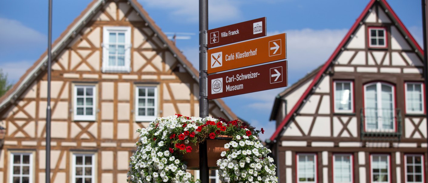 Ein Wegweiser mit Blumen vor Fachwerkhäusern auf dem Marktplatz von Murrhardt. Schilder zeigen zu Villa Franck, Café Klosterhof und Carl-Schweizer-Museum., © Stuttgart-Marketing GmbH, Achim Mende