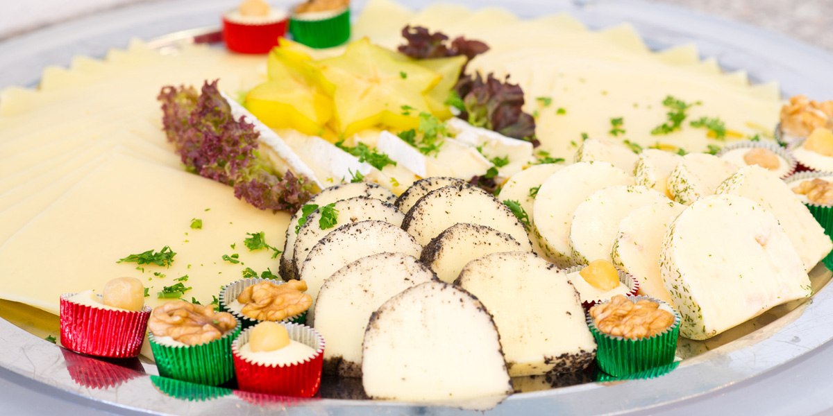 Käseplatte mit verschiedenen Käsesorten, dekoriert mit Nüssen, Obst und Kräutern auf einem silbernen Tablett., © ACHAT Hotels Deutschland