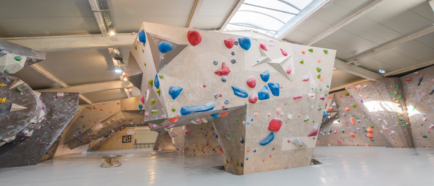 Innenansicht der VELS Boulderhalle mit Kletterwänden und bunten Griffen unter einem gewölbten Dach., © Boulderhalle Vels Innenansicht der VELS Boulderhalle mit Kletterwänden und bunten Griffen unter einem gewölbten Dach., © Boulderhalle Vels