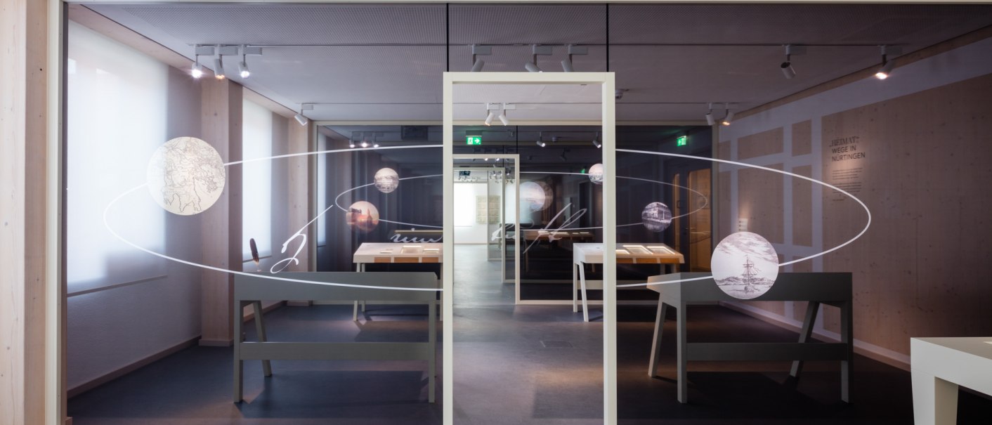 Moderne Ausstellung mit Glastrennwand, dekorativen Kreisen und Tischen. Die Wand zeigt stilisierte Linien und Kreise, die den Raum optisch teilen., © dieargelola, Stuttgart