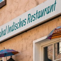 Fassade eines indischen Restaurants in Stuttgart mit bunten Schirmen und einem Schild mit der Aufschrift 'Taj Mahal Indisches Restaurant'., © SMG, Sarah Schmid Fassade eines indischen Restaurants in Stuttgart mit bunten Schirmen und einem Schild mit der Aufschrift 'Taj Mahal Indisches Restaurant'., © SMG, Sarah Schmid