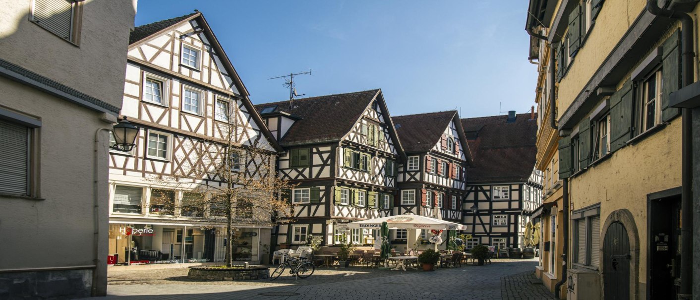 Fachwerkhäuser am Marktplatz in Schorndorf, sonniger Tag, leere Straße, ein Fahrrad steht vor einem Café mit Sonnenschirmen., © SMG, Sarah Schmid