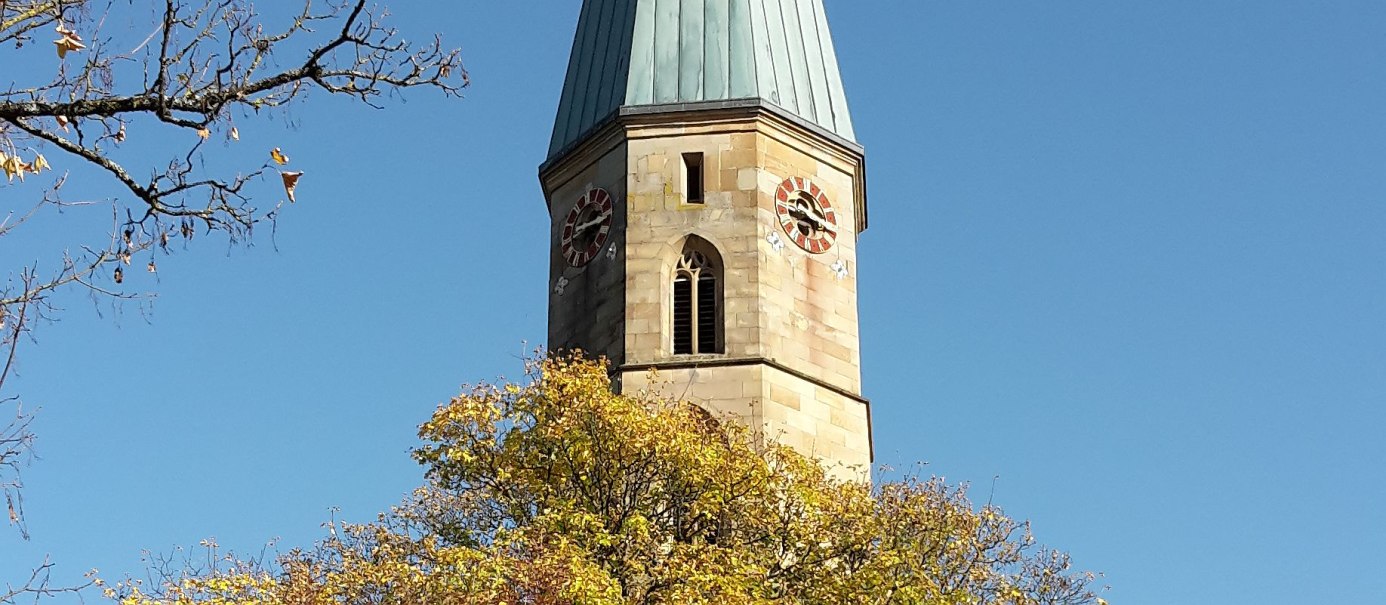 Kirchturm der Stadtkirch - Bildausschnitt mit gotischem Fenster und Turmuhr, im Vordergrund Baumkuppe mit gelbem Herbstlaub, © Petra Natzkowski