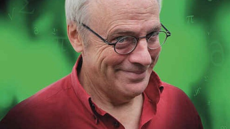 Ein Mann mit Brille und rotem Hemd l&auml;chelt vor einem gr&uuml;nen Hintergrund mit mathematischen Symbolen. Er wirkt freundlich und nachdenklich., &copy; Mauerwerk GmbH