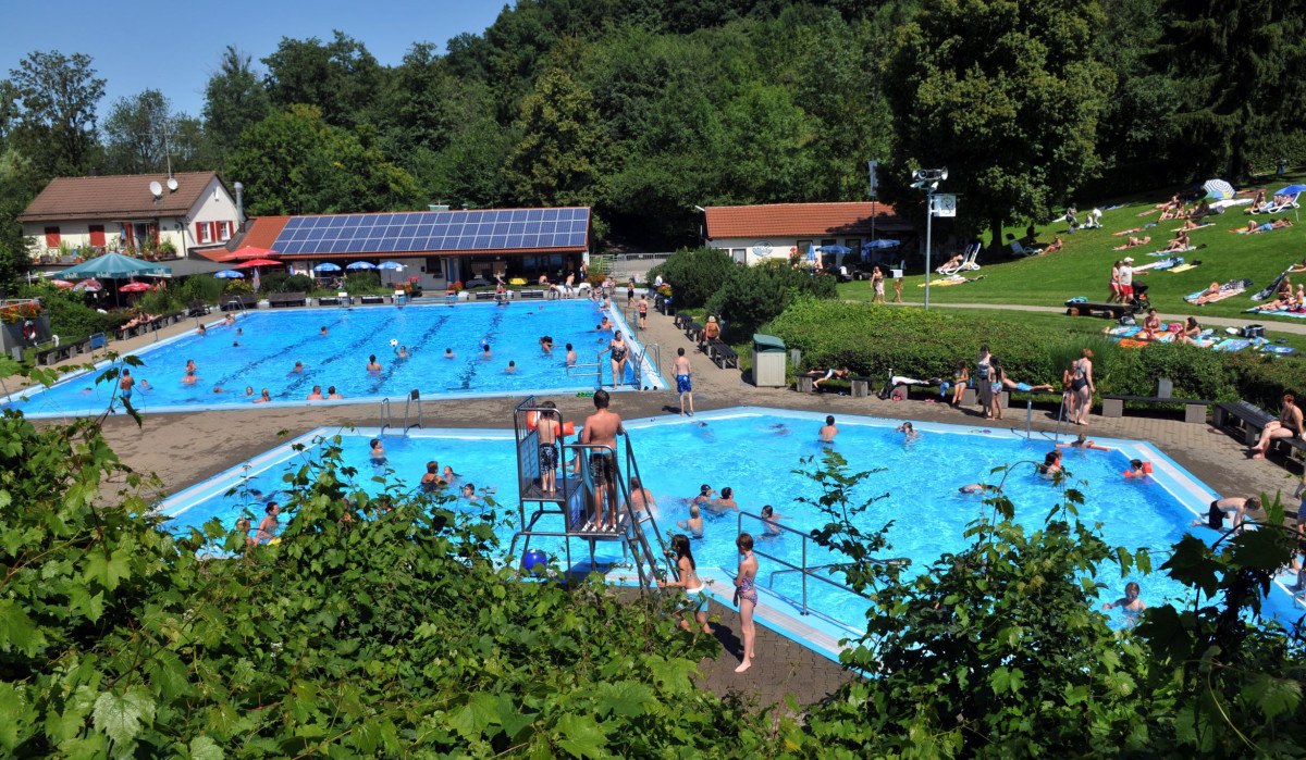 Ein Freibad mit vielen Besuchern im Wasser und auf der Liegewiese. Im Hintergrund sind Bäume und ein Gebäude mit Solarpanelen zu sehen., © Gemeinde Bad Boll Ein Freibad mit vielen Besuchern im Wasser und auf der Liegewiese. Im Hintergrund sind Bäume und ein Gebäude mit Solarpanelen zu sehen., © Gemeinde Bad Boll
