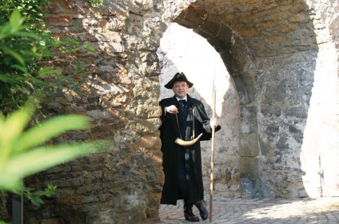 Ein Mann in historischer Kleidung mit Hut und Horn steht unter einem alten Steinbogen und zeigt in die Kamera., © WTM GmbH Waiblingen Ein Mann in historischer Kleidung mit Hut und Horn steht unter einem alten Steinbogen und zeigt in die Kamera., © WTM GmbH Waiblingen