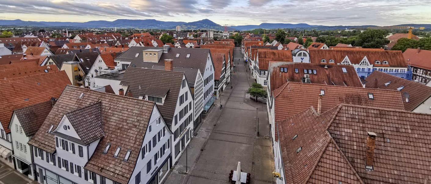 Panoramablick auf die roten Ziegeldächer von Kirchheim unter Teck, mit einer leeren Straße und Bergen im Hintergrund unter bewölktem Himmel., © Torsten Wenzler Panoramablick auf die roten Ziegeldächer von Kirchheim unter Teck, mit einer leeren Straße und Bergen im Hintergrund unter bewölktem Himmel., © Torsten Wenzler