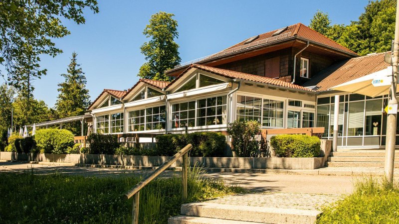 Ein modernes Geb&auml;ude mit gro&szlig;en Fenstern und rotem Dach, umgeben von B&auml;umen und Gr&uuml;nfl&auml;chen. Der Himmel ist klar und blau., &copy; Stuttgart-Marketing GmbH, Sarah Schmid