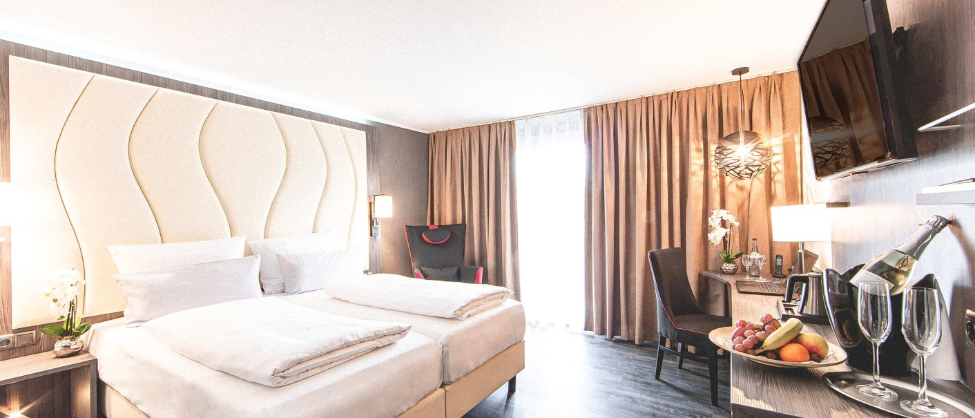 Modernes Hotelzimmer mit Doppelbett, stilvollem Kopfteil, Schreibtisch, Fernseher, Obstteller und Champagner auf einem Tisch., © Plaza Residence Stuttgart-Ditzingen Modernes Hotelzimmer mit Doppelbett, stilvollem Kopfteil, Schreibtisch, Fernseher, Obstteller und Champagner auf einem Tisch., © Plaza Residence Stuttgart-Ditzingen