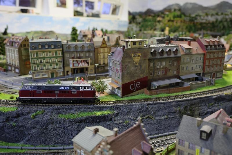 Eine detaillierte Modellbahnlandschaft mit einem roten Zug und Gebäuden. Die Szene zeigt eine Stadt mit Straßen und Häusern im Miniaturformat., © Backnang