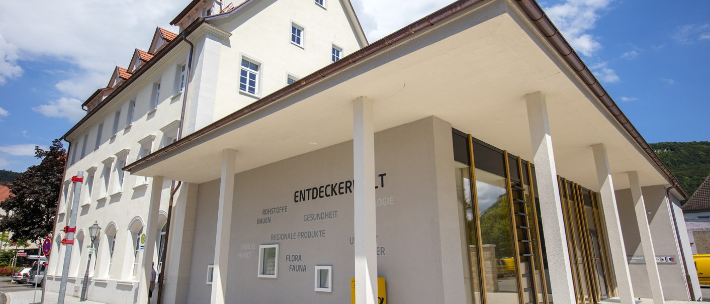 Modernes Gebäude mit der Aufschrift 'Entdeckerwelt' in Bad Urach, helle Fassade, große Fenster, blauer Himmel im Hintergrund., © Bad Urach Tourismus