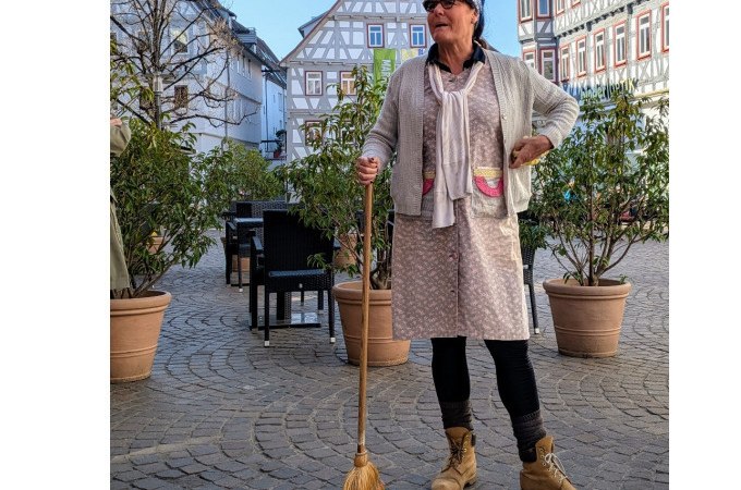 Eine Frau in traditioneller Kleidung mit Besen steht auf einem gepflasterten Platz vor Fachwerkhäusern. Sie trägt eine Mütze und Sonnenbrille., © WTM GmbH Waiblingen Eine Frau in traditioneller Kleidung mit Besen steht auf einem gepflasterten Platz vor Fachwerkhäusern. Sie trägt eine Mütze und Sonnenbrille., © WTM GmbH Waiblingen