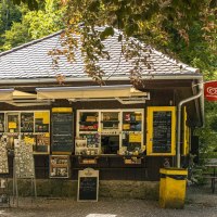 Ein Kiosk im Wald mit Verkaufstafeln und Sitzbänken. Langnese-Flaggen hängen an den Seiten. Der Weg führt durch die grüne Umgebung., © Stuttgart-Marketing GmbH, Sarah Schmid Ein Kiosk im Wald mit Verkaufstafeln und Sitzbänken. Langnese-Flaggen hängen an den Seiten. Der Weg führt durch die grüne Umgebung., © Stuttgart-Marketing GmbH, Sarah Schmid