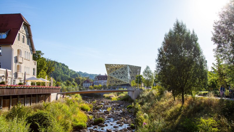 Moderne Architektur im Remspark, umgeben von Natur. Ein Fluss mit Brücke im Vordergrund, Bäume und ein Gebäude links., © Mario Klaiber Moderne Architektur im Remspark, umgeben von Natur. Ein Fluss mit Brücke im Vordergrund, Bäume und ein Gebäude links., © Mario Klaiber