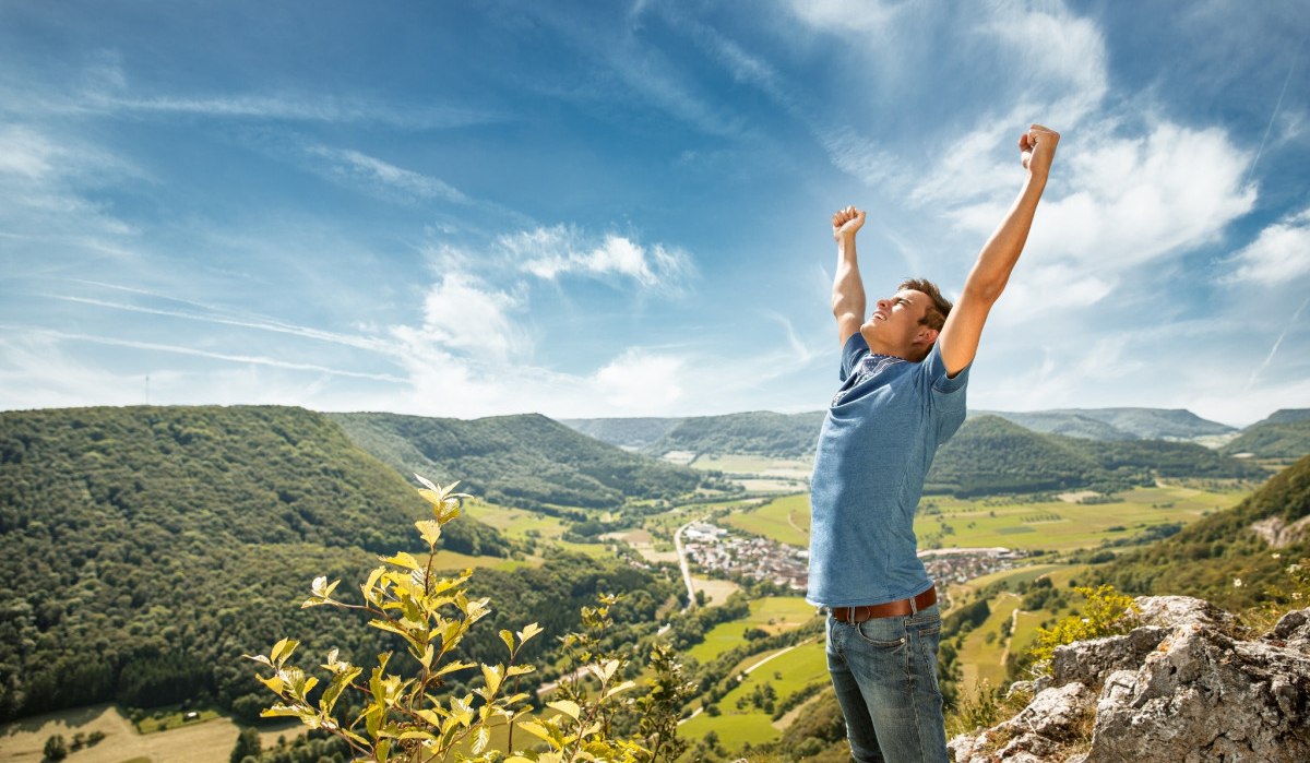 Mann auf Felsen mit erhobenen Armen, blickt über grüne Hügel und ein Dorf im Tal. Klarer Himmel, sonniger Tag., © Landkreis Göppingen Mann auf Felsen mit erhobenen Armen, blickt über grüne Hügel und ein Dorf im Tal. Klarer Himmel, sonniger Tag., © Landkreis Göppingen