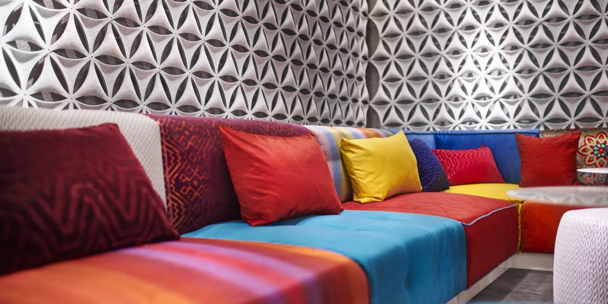 Bunte Sofas mit roten, gelben und blauen Kissen vor einer geometrisch gemusterten Tapete in einer Lobby., © Jaz Hotel Stuttgart