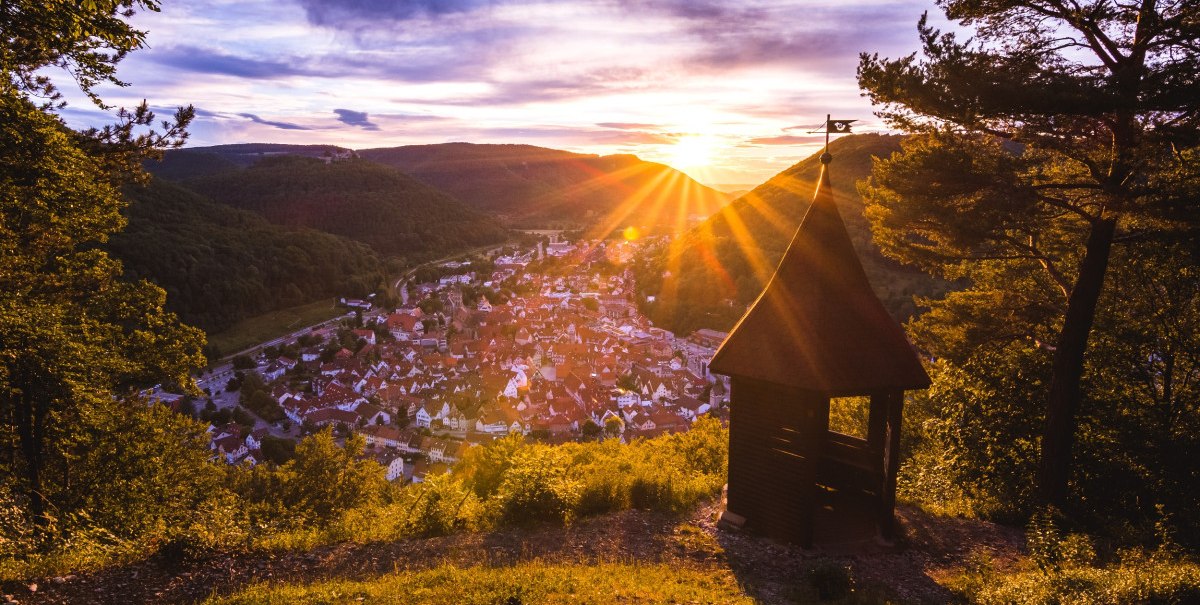Sonnenuntergang über einem Dorf, gesehen von einem Hügel mit einer kleinen Holzhütte im Vordergrund. Die Sonne strahlt über die Landschaft., © Bad Urach Tourismus Sonnenuntergang über einem Dorf, gesehen von einem Hügel mit einer kleinen Holzhütte im Vordergrund. Die Sonne strahlt über die Landschaft., © Bad Urach Tourismus