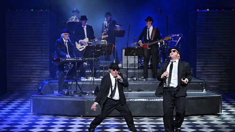 Bühnenauftritt der Blues Brothers mit Band in Anzügen und Hüten. Zwei Sänger im Vordergrund, Musiker im Hintergrund auf einer erhöhten Plattform., © Stadt Remseck am Neckar
