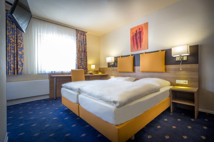 Ein gemütliches Doppelzimmer mit einem großen Bett, Schreibtisch, Fernseher und dekorativer Kunst an der Wand., © Römerhof Hotelbetriebs GmbH