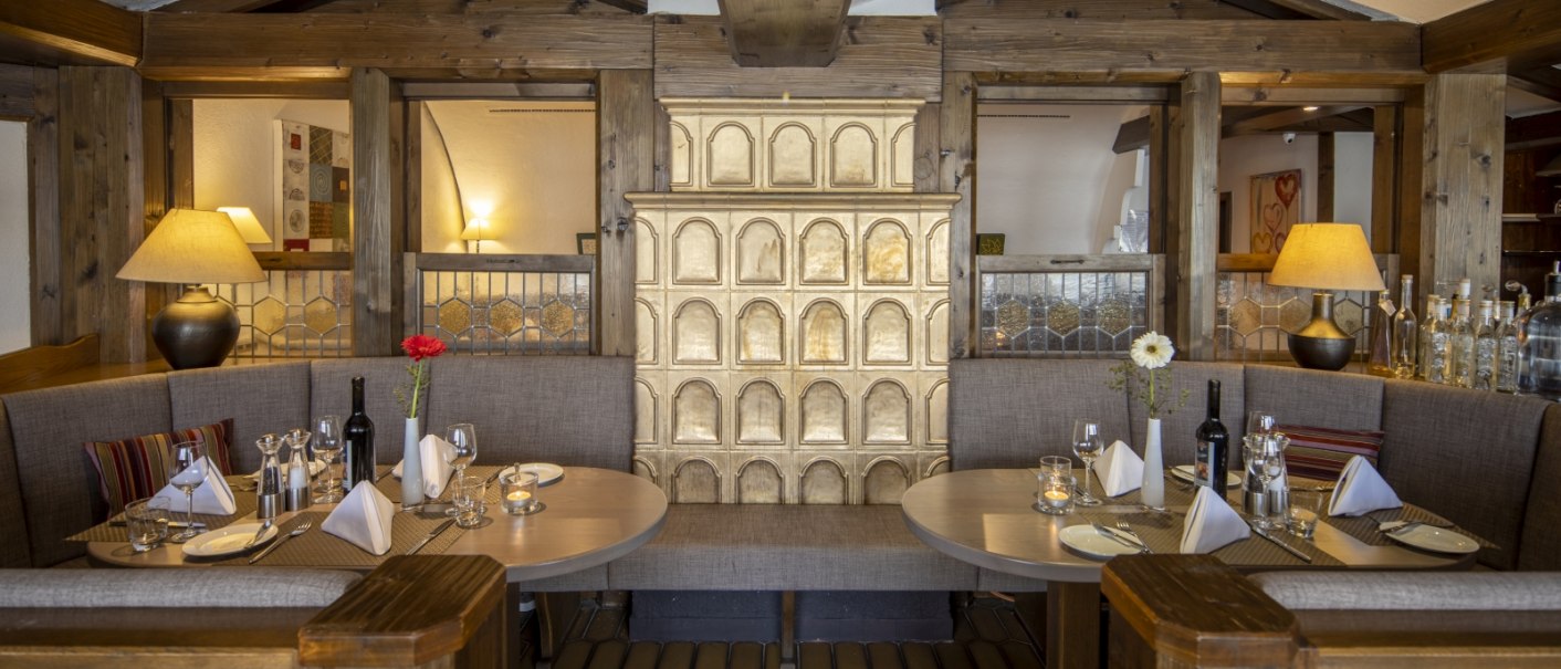 Gem&uuml;tliche Restaurant-Ecke mit Holztischen, gedeckten Pl&auml;tzen und einem dekorativen Kachelofen in der Mitte., &copy; Hotel Gloria GmbH