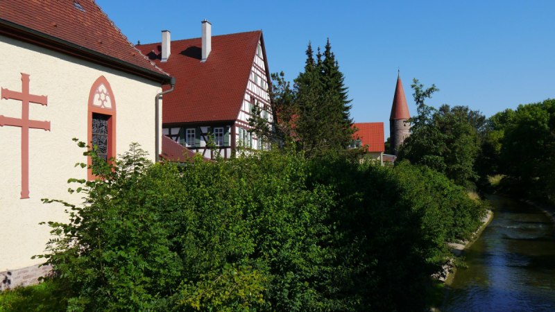 Fachwerkhaus und Kirche mit Turm an einem Flussufer, umgeben von Bäumen und blauem Himmel., © Natur.Nah. Schönbuch & Heckengäu Fachwerkhaus und Kirche mit Turm an einem Flussufer, umgeben von Bäumen und blauem Himmel., © Natur.Nah. Schönbuch & Heckengäu